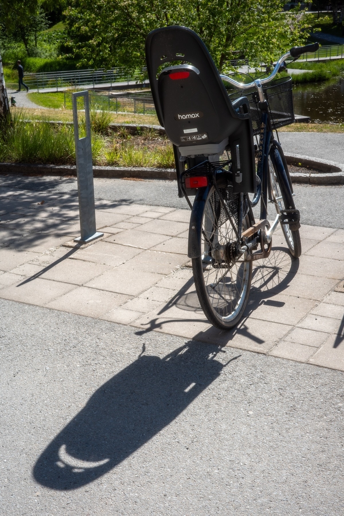 A bicycle with a child seat mounted on the back parked on a paved path in a park. A shadow of the bicycle and child seat is cast on the ground.