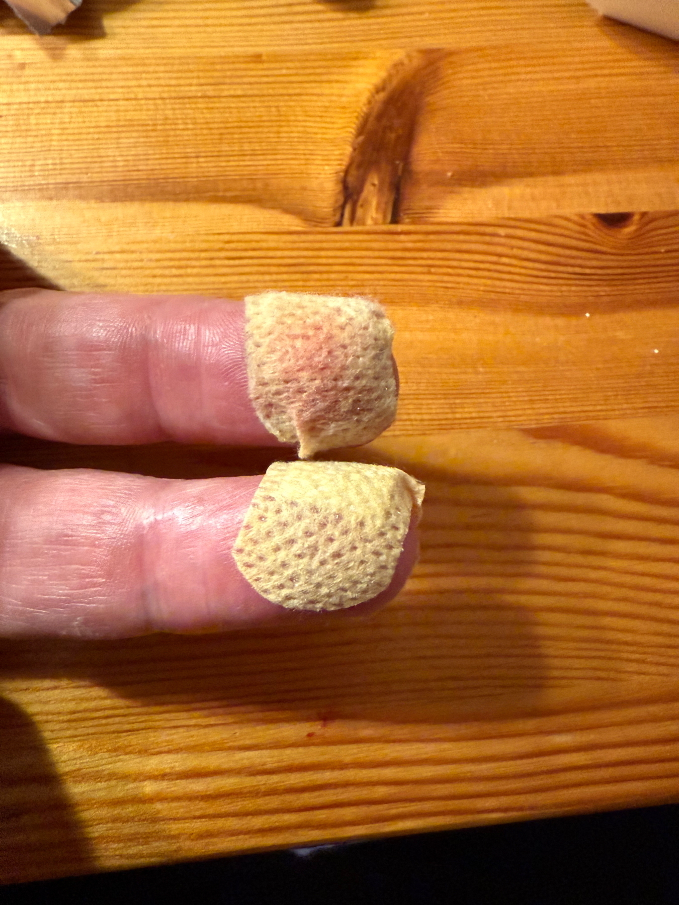 Two fingers with beige band-aids on the tips, resting on a wooden surface.