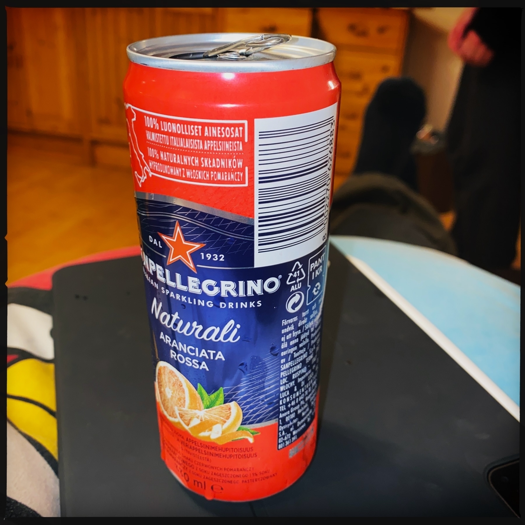 A can of San Pellegrino sparkling drink, specifically “Aranciata Rossa” (blood orange flavor), featuring a vibrant design with a red and blue color scheme and orange slice illustrations. The text on the can mentions “100% luonnoll