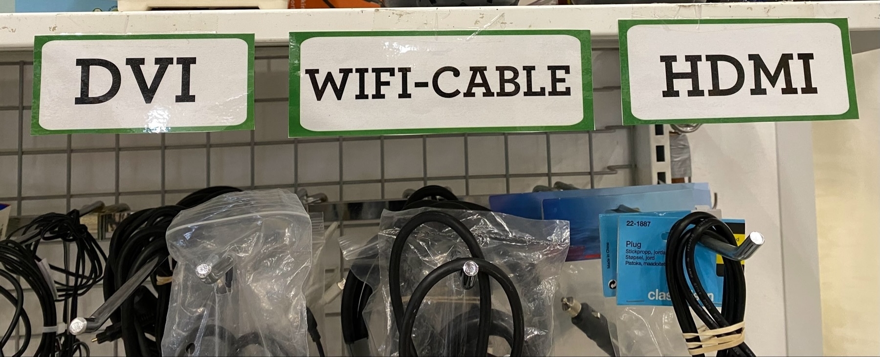 The image shows a display shelf with three labeled sections for different types of cables. The labels read “DVI,” “WIFI-CABLE,” and “HDMI.” Various cables are hanging under each label, with some cables in plastic bags.