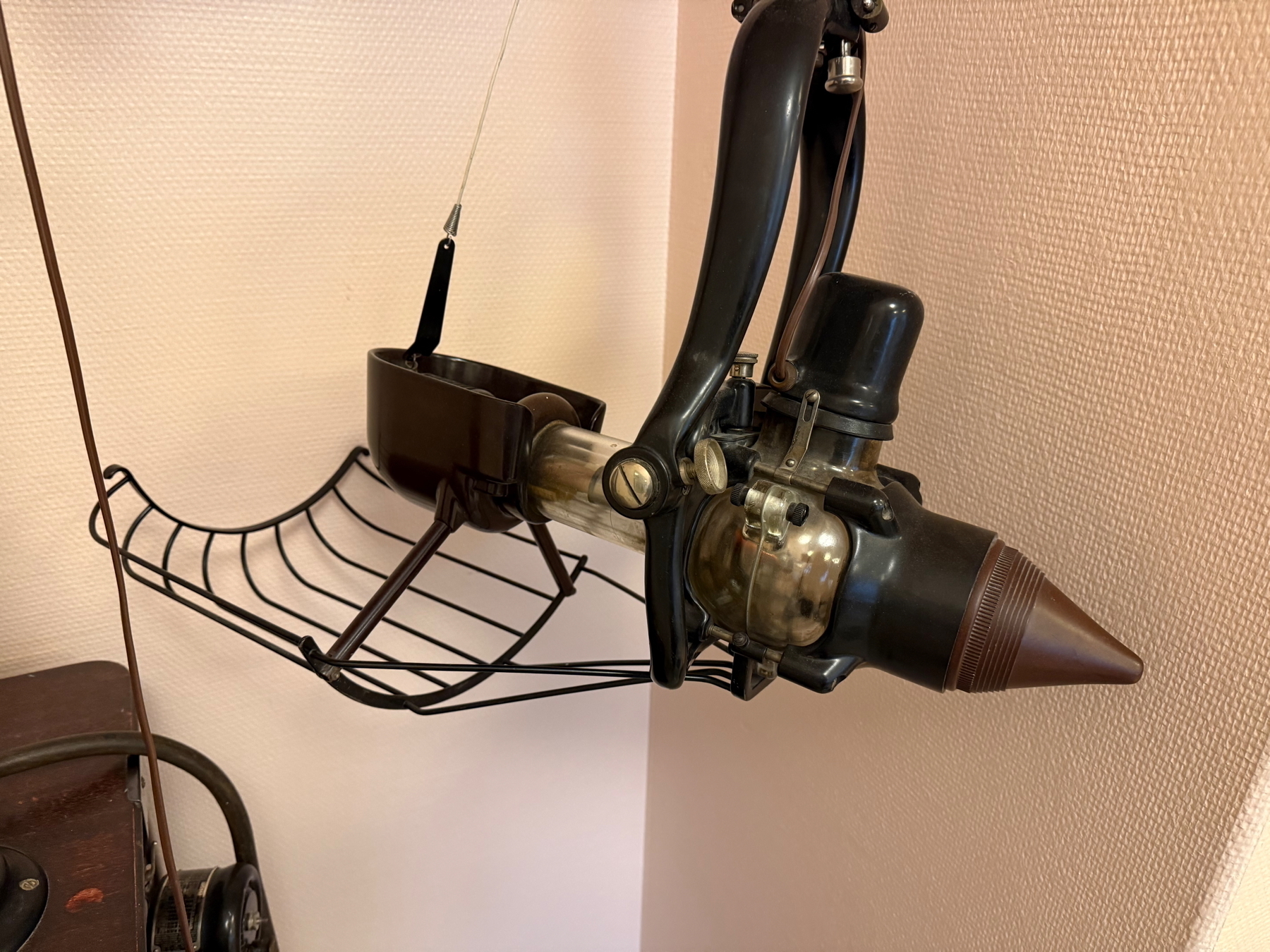 A vintage dental x-ray machine with an arm and cone-shaped attachment, mounted on a metal stand with a wire frame.